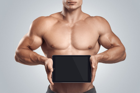Close up photo of a handsome young fitness male model holding horizontally digital tablet with blank screen, isolated on white backgroundの写真素材