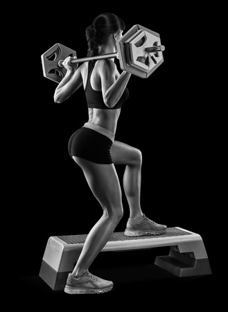 Strong young woman with beautiful athletic body doing exercises with barbell. Black and white photoの写真素材
