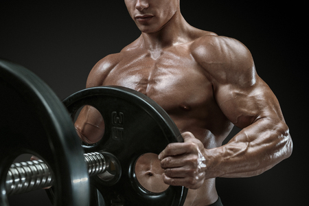 Closeup photo of handsome bodybuilder guy prepare to do exercises with barbell in a gym, keep barbell plate in handsの写真素材