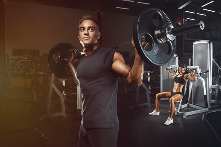 Young and fit couple in the gym doing workout. Group of women and men bodybuilders training on special sport equipment in the gym. Sport, bodybuilding, lifestyle and people concept.の写真素材