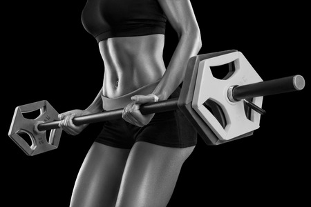 Beautiful young woman exercises with barbell isolated over black background. Black and white photo.の写真素材