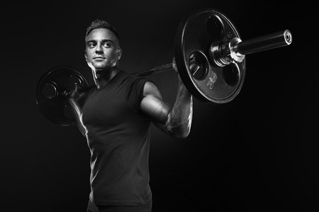 Closeup portrait of professional bodybuilder workout with barbell on black background. Black and white photo. Muscular man training squats with barbells over headの写真素材