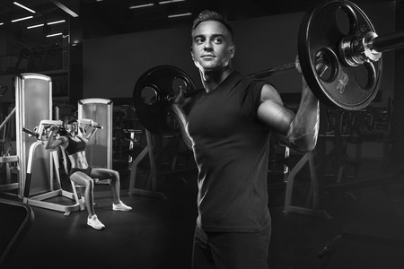 Young and fit couple in the gym doing workout. Group of women and men bodybuilders training on special sport equipment in the gym. Sport, bodybuilding, lifestyle and people concept. Black and white photo.の写真素材