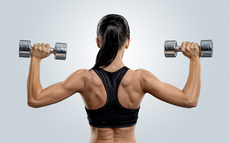 Fitness sporty woman in training pumping up muscles of the back and hands with dumbbellsの写真素材