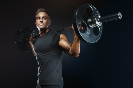Closeup portrait of professional bodybuilder workout with barbell on black background. Muscular man training squats with barbells over headの写真素材