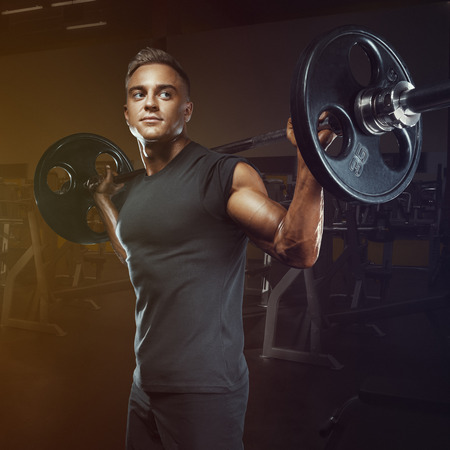 Confident muscular man training squats with barbells over head. Closeup portrait of professional bodybuilder workout with barbell at gym.の写真素材