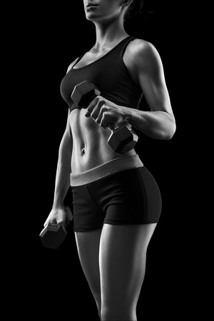 Fitness sporty woman in training pumping up muscles with dumbbells. Young sports sexy fitness woman body with dumbbells posing on black background, isolated.の写真素材