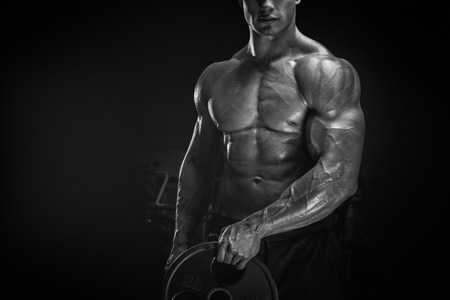 Close up photo of power athletic man doing exercises with barbell plate. Muscular body on dark background.の写真素材