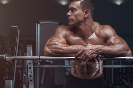 Attractive muscular bodybuilder guy prepare to do exercises with barbell in a gymの写真素材