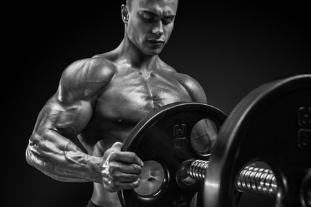 Handsome bodybuilder guy prepare to do exercises with barbell in a gym, keep barbell plate in handsの写真素材