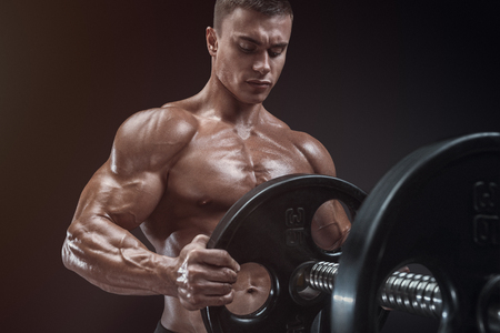 Handsome bodybuilder guy prepare to do exercises with barbell in a gym, keep barbell plate in handsの写真素材