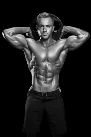 Perfect fit athletic guy posing with barbell plate in gym, perfect lat muscle, shoulders, biceps, triceps and chest. Fitness muscular body isolated on dark background.の写真素材