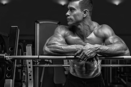 Attractive muscular bodybuilder guy prepare to do exercises with barbell in a gym. Black and white portrait.の写真素材