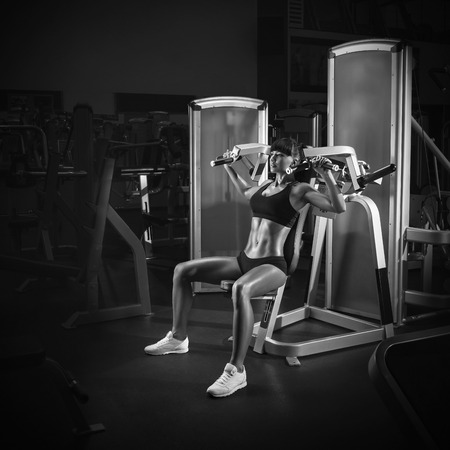 Strong young woman with beautiful athletic body doing exercises special sport equipment in the gym. Black and white photoの写真素材