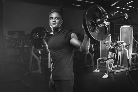 Young and fit couple in the gym doing workout. Group of women and men bodybuilders training on special sport equipment in the gym. Sport, bodybuilding, lifestyle and people concept. Black and white photo.の写真素材