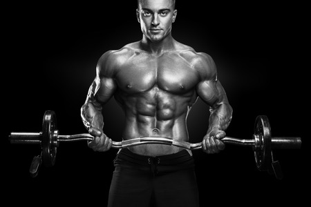 Portrait of handsome bodybuilder performing the biceps curl with EZ curl bar at gym. Perfect physique athletic young man with six pack, perfect abs, shoulders, biceps, lats and chest.の写真素材