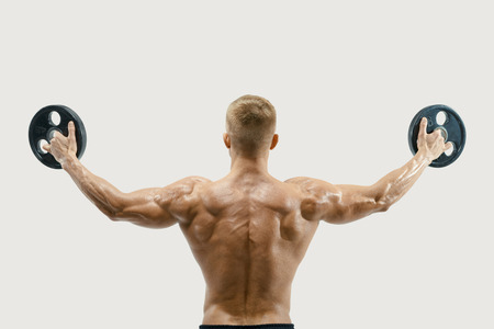 Rear view of young bodybuilder lifting weights rising hands against white background. Fit and muscles sportsman exercising with barbell plate turning back.の写真素材