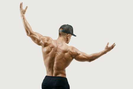 Shot of healthy muscular young man turning back and rise both hands. Perfect fit, six pack, abs,...