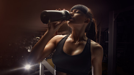 Fitness woman drinking water from bottle. Muscular young female at gym taking a break from workout.の写真素材
