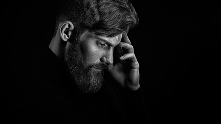 Black and white portrait of young handsome bearded man with stylish haircut thinking in deciding in profile on dark studio background, copy spaceの写真素材
