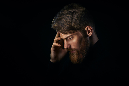 Close-up portrait of young handsome bearded man with stylish haircut thinking in deciding in profile on dark studio background, copy spaceの写真素材