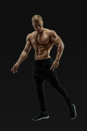 Full-length shot of handsome young man with muscular body standing against black background. Perfect fit, six pack, abs, abdominal muscle, shoulders, deltoids, biceps. Vector mask clipping pathの写真素材