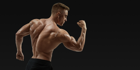 Strong back of a athletic muscular man flexing his arms against black background. Rear view of  handsome young shirtless fitness model with masculine physique in full-length silhouette. Vector clipping path maskの写真素材
