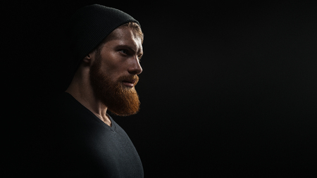 Silhouette of young confident handsome bearded man hipster wearing black knit hat. Studio shot on dark background Image with free copy spaceの写真素材