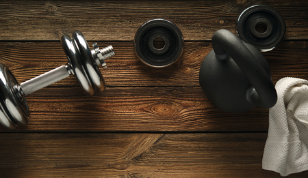Top view of black iron kettlebell, dumbbell and white towel on wooden floor Sport background with copyspace  Weight lifting exercise concept.の写真素材