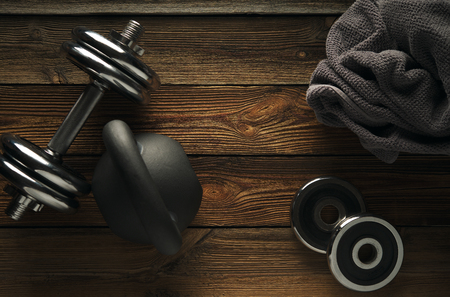 Top view of black iron kettlebell, dumbbell and grey towel on wooden floor Sport background with copyspace  Healthy diet and fitness conceptの写真素材