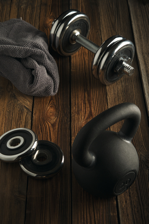 Top view of black iron kettlebell, dumbbell and grey towel on wooden floor Sport background with copyspace  Healthy diet and fitness conceptの写真素材