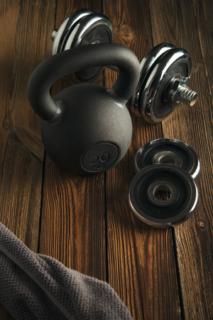 Top view of black iron kettlebell, dumbbell and grey towel on wooden floor Sport background with copyspace  Healthy diet and fitness conceptの写真素材