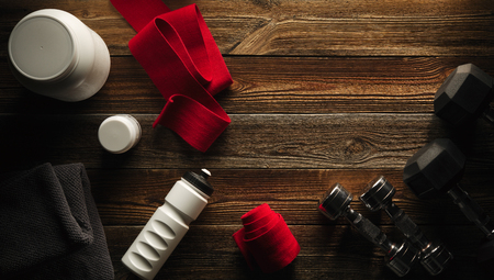 Grey towel Protein shake bottle Dumbbells White jar with whey protein Red hand wrap on wooden floor Gym background Sport fitness bodybuilding healthy lifestyle and weightlifting conceptの写真素材