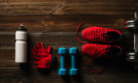 Top view Fitness equipment and supplements on wooden floor in gym Fitness background with Pair of Sneakers White water bottle Steel dumbbell and Pair of red glovesの写真素材