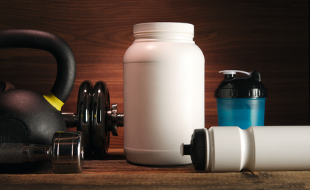Grey towel Protein shake bottle Dumbbell plate White jar with whey protein Red hand wrap Sneakers on wooden floor Gym background Sport fitness bodybuilding healthy lifestyle and weightlifting conceptの写真素材