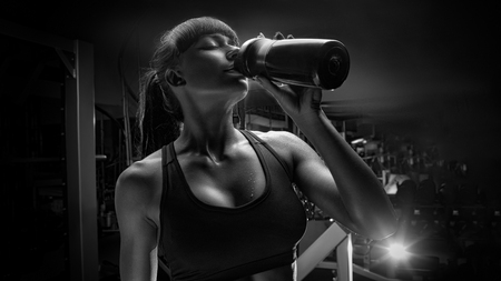 Black and white photo of fitness woman drinking water from bottle. Muscular young female at gym taking a break from workout.の写真素材