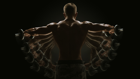 Fitness Sport Lifestyle Dumbbell Lateral Raise concept Bodybuilder turning back raising hands pumping up shoulders muscle exercise Power Partials routine with dumbbells on gym Dramatic studio shotの写真素材