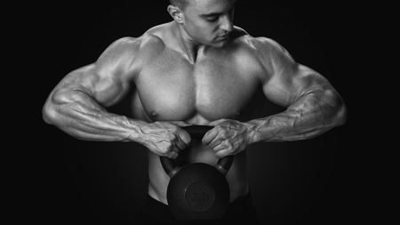 Black and white photo of shirtless young athlete with muscular body exercising crossfit with kettle bell on black background Intensive cross trainingの写真素材