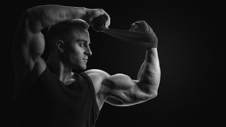 Black and white photo of man is wrapping hands with boxing wraps isolated on black background Strong hands and fist, ready for training and active exerciseの写真素材