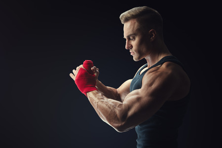 Strong man wrap hands on black background Man is wrapping hands with red boxing wraps isolated on black background Strong hands and fist, ready for training and active exerciseの写真素材