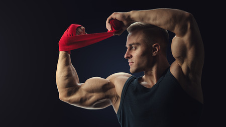 Strong man wrap hands on black background Man is wrapping hands with red boxing wraps isolated on black background Strong hands and fist, ready for training and active exerciseの写真素材