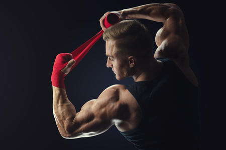 Strong man wrap hands on black background Man is wrapping hands with red boxing wraps isolated on black background Strong hands and fist, ready for training and active exerciseの写真素材