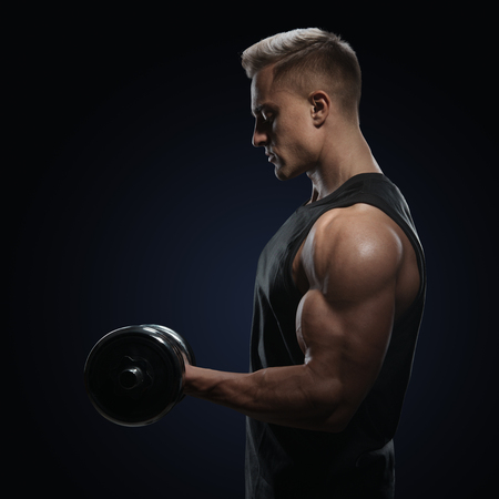 Athletic man in training pumping up muscles with dumbbell. Strong bodybuilder with perfect deltoid muscles, shoulders, biceps, triceps and chest. Close-up of a power fitness man.の写真素材