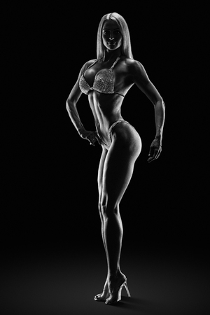 Black and white dramatic photo Fitness bikini model competition championship Female athlete bodybuilder posing on stage Perfect trained body shape legs arms chest Strong muscular sports Clipping pathの写真素材