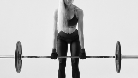 Close-up black and white image of young fitness woman doing weight lifting workout Attractive young woman bodybuilder lifting barbells Horizontal black and white concept photo focused on barbellの写真素材