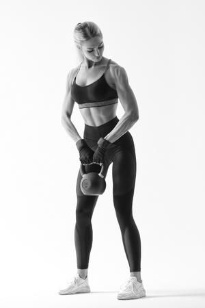Caucasian fitness model working out with kettlebell in black sportswear Full length black and white shot of young muscular female bodybuilder doing heavy kettlebell exercise for deltoidsの写真素材