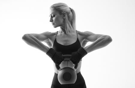Fitness woman workout with kettlebell training Waist-up black and white portrait of attractive young fitness woman focused on workout with kettle bell Isolated on white backgroundの写真素材