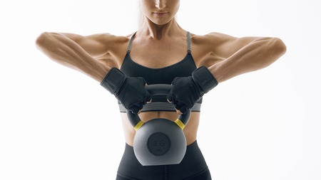 Cropped shot of female bodybuilder in sportswear doing crossfit workout with kettle bell on white background Confident looking forward young athlete with muscular body exercising crossfitの写真素材