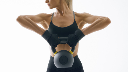 Cropped shot of young woman in sportswear exercise with kettlebell Strong fitness female exercising with heavyweights isolated on white background Female model with muscular and slim bodyの写真素材