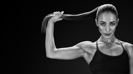 Beautiful young fit sexy woman in sportswear holding her ponytail Strong healthy hair Clipping path Female bodybuilder with power hand confidental looking forward Black and white photo.の写真素材
